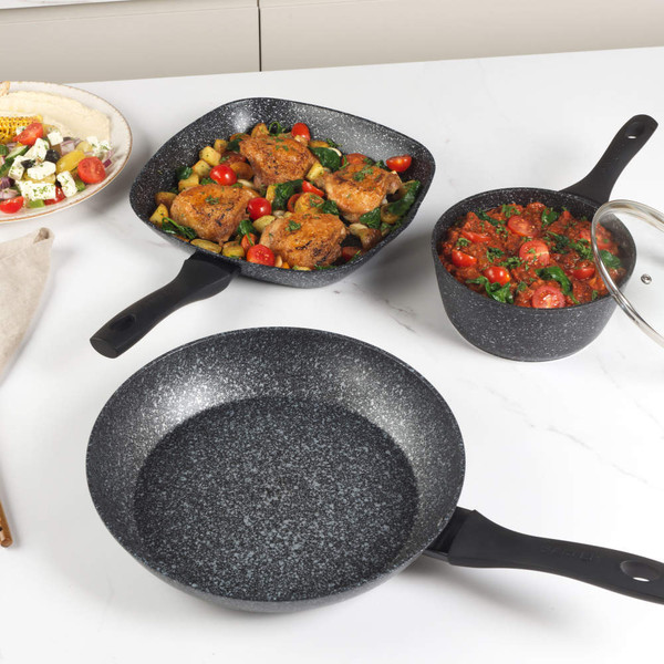 Set of three black and white speckled non-stick pans, two with cooked food, on a white kitchen counter