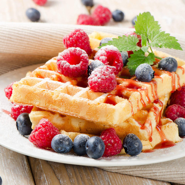 Two waffles topped with raspberries, blueberries and icing sugar on a plate