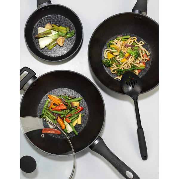 Set of three black non-stick woks with assorted stir-fried vegetables, shown from above.