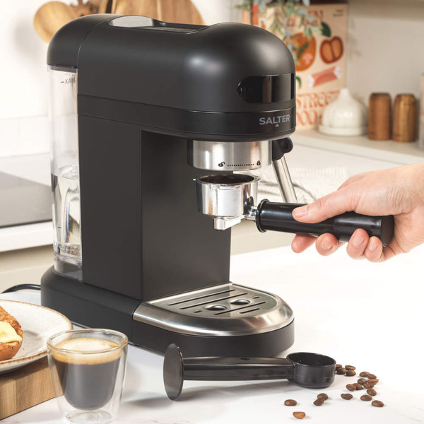 Portafilter with ground coffee and tamper on white surface, some coffee spilled
