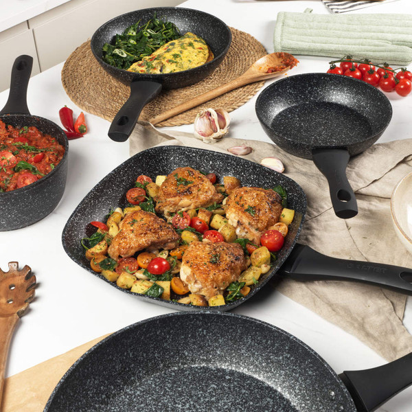 Set of black speckled non-stick saucepans and frying pan with glass lids on kitchen worktop