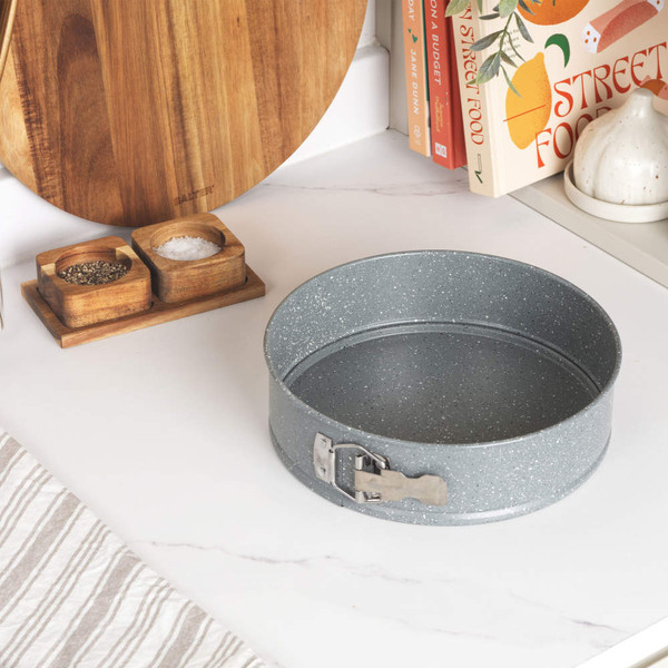 Round speckled grey springform cake tin shown with other baking trays