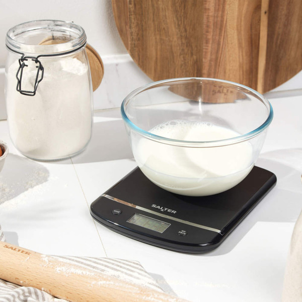 Glass bowl with milk on black Salter kitchen scale, baking ingredients nearby