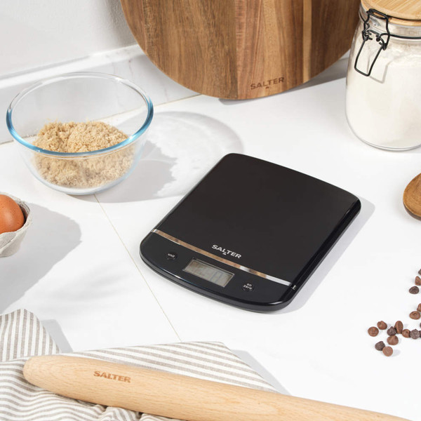 Digital kitchen scale with glass bowl of milk on top, shown on kitchen counter