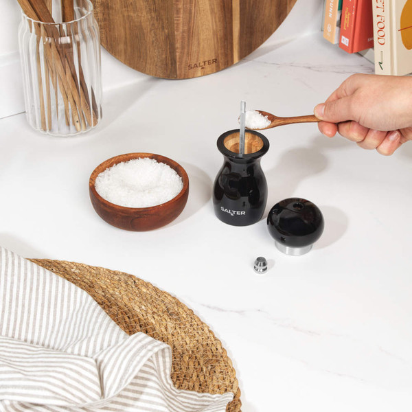 Black wooden pepper mill held in both hands, showing the grinder underside.