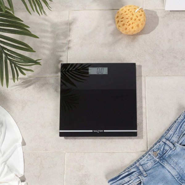 Black digital bathroom scale displaying weight, top-down view, in home setting