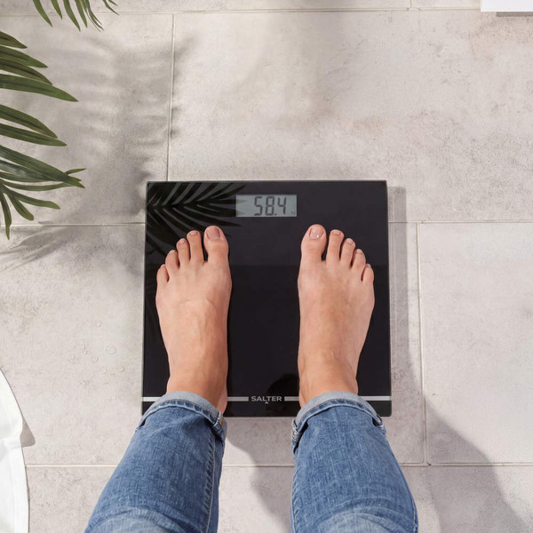 Person standing on black digital bathroom scale, weight display reads 58.4 kg