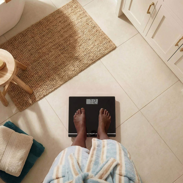 Bathroom digital scale, black glass with clear display, shown on tiled floor
