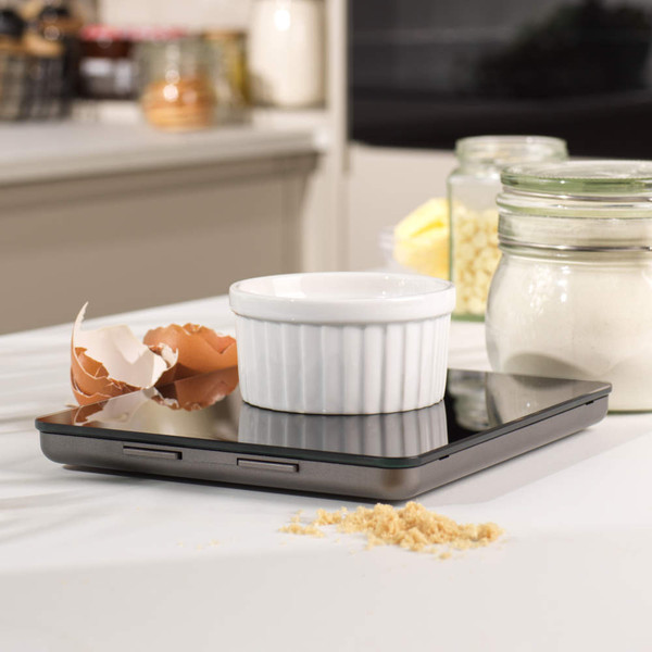 Black digital kitchen scale on worktop with eggs, chocolate and rolling pin