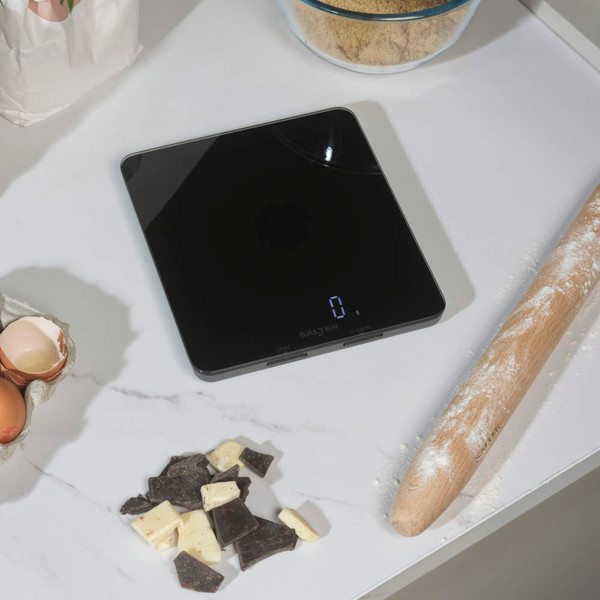 Glass bowl of brown sugar on digital kitchen scale, hand holding bowl, baking scene