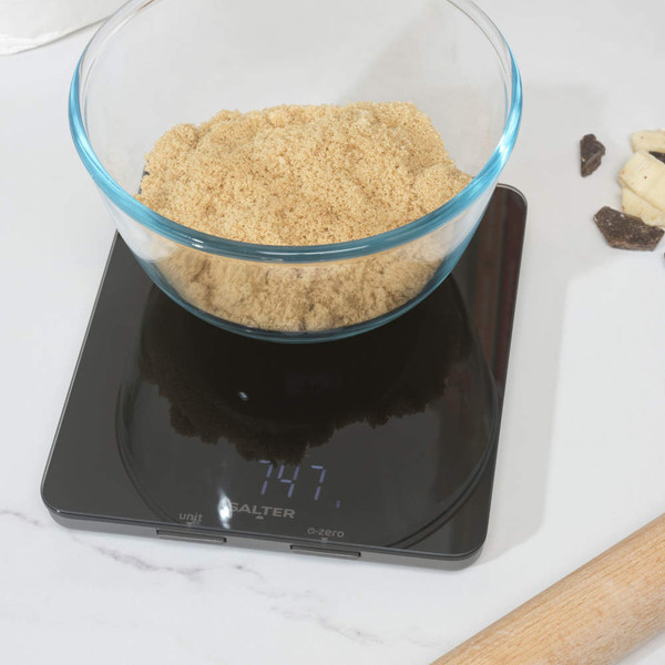 Glass bowl of brown sugar on a digital kitchen scale showing 747 grams.