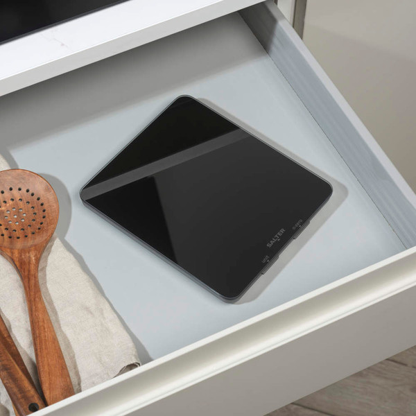 Black digital kitchen scale with a white ramekin and eggshells on top, on a countertop