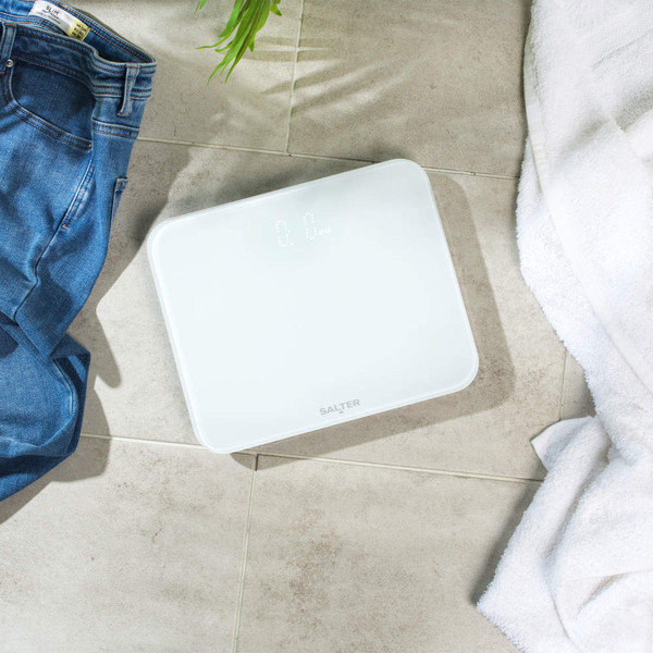 White Salter digital bathroom scale on tiled floor, shown with jeans and towel.