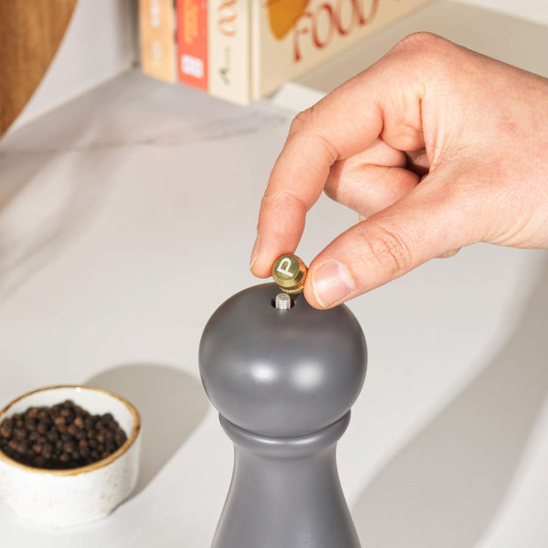 Hand adjusting black pepper mill, bowl of peppercorns in background