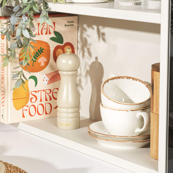 Beige Salter pepper mill on shelf beside stacked rustic cups and Italian recipe book