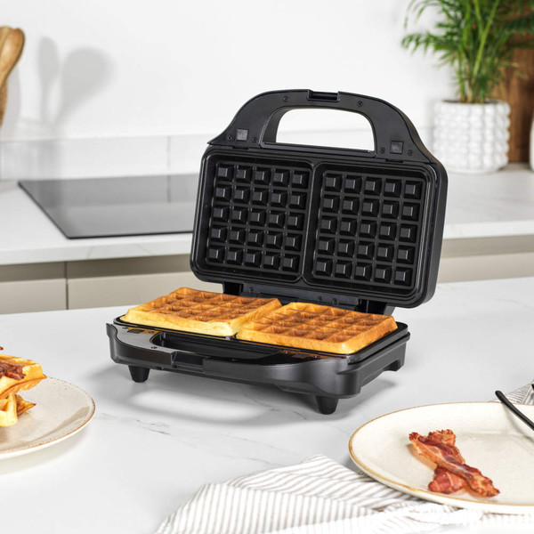 Black waffle maker with two cooked square waffles on kitchen worktop