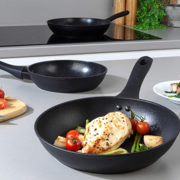 Black non-stick frying pan with chicken and vegetables, on a kitchen counter