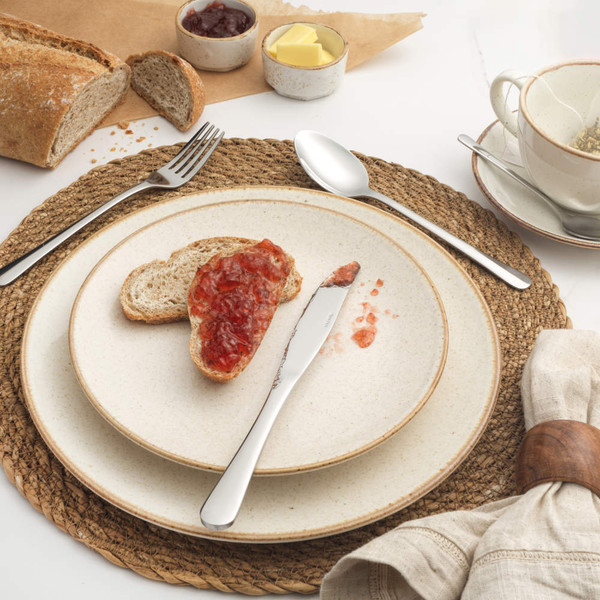 Set of four silver stainless steel cutlery pieces on stone-coloured plate, fork, knife, spoon, teaspoon