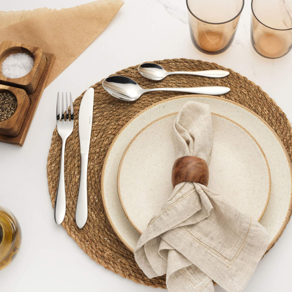 Table setting with neutral ceramic plates, linen napkin in wooden ring, silver cutlery and woven placemat.