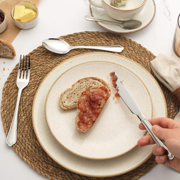 Slice of bread with jam on plate, hand holding knife, breakfast table setting