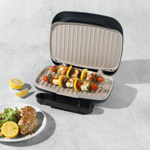 Electric grill with open lid showing vegetable and halloumi skewers on plates