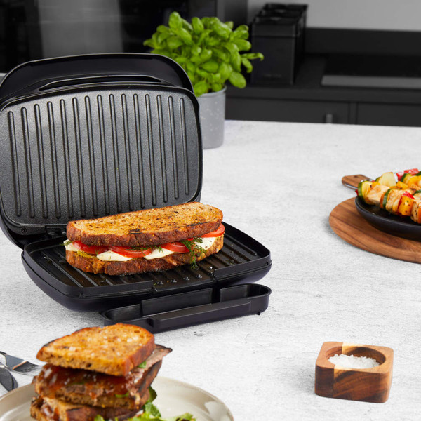 Black sandwich maker with grilled cheese and tomato toastie on kitchen countertop