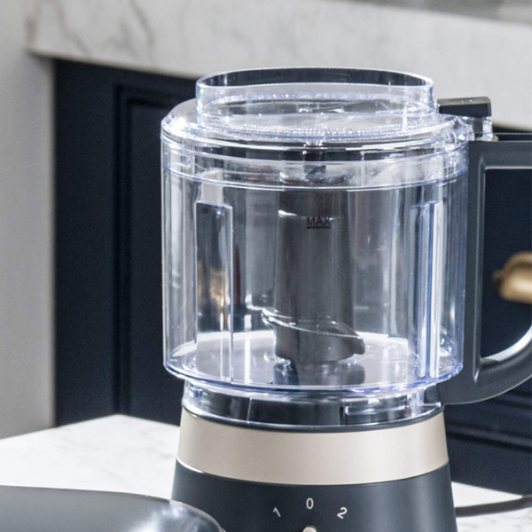 Food processor with avocado, walnuts, and garlic, oil being poured in through lid