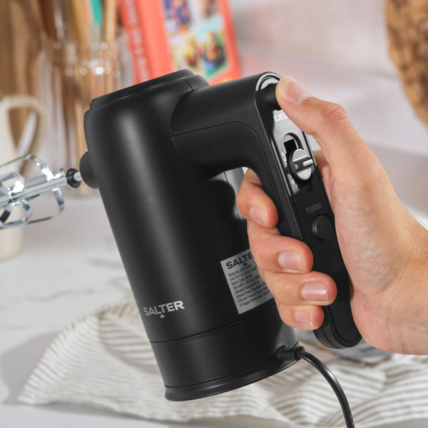 Black hand mixer blending batter in glass bowl, shown from above