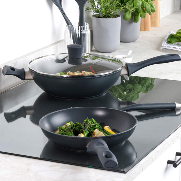 Non-stick frying pan and wok with food on induction hob, kitchen setting