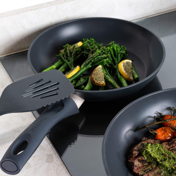 Black frying pan with grilled broccoli and lemon wedges on induction hob
