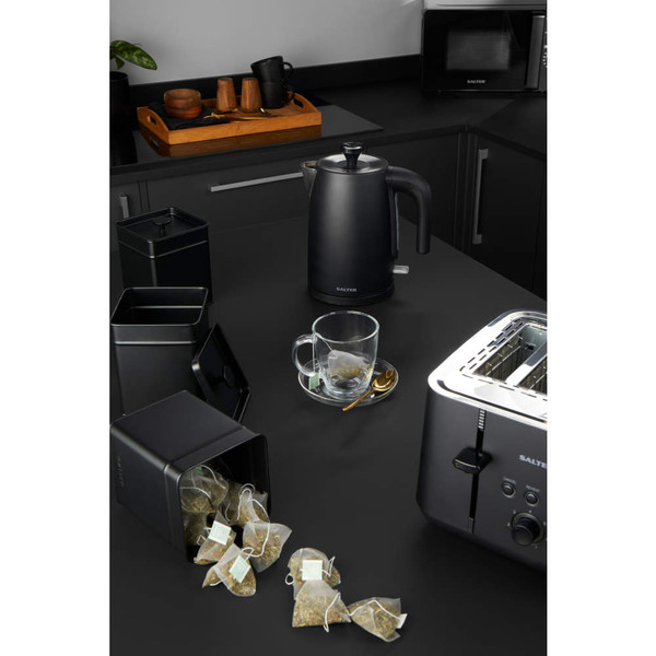 Black kettle, toaster, and tea caddy in modern kitchen with glass mug and loose teabags