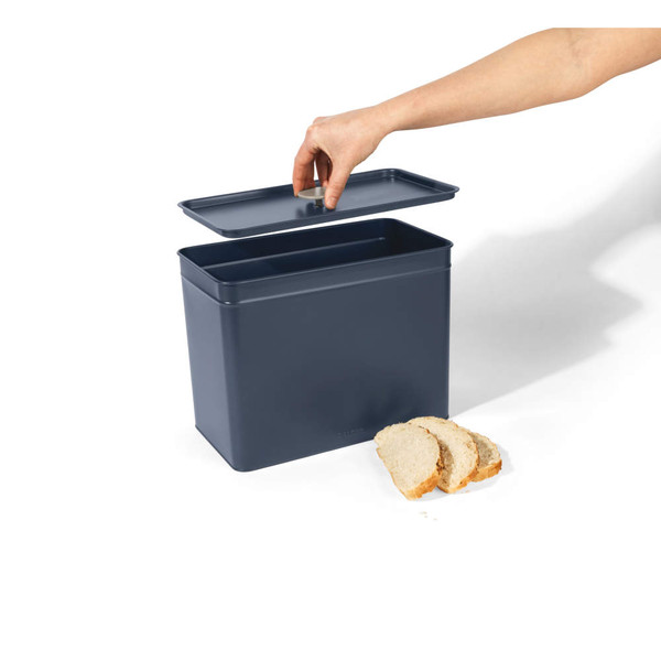 Navy blue bread bin with lid being lifted, with three slices of bread in front.