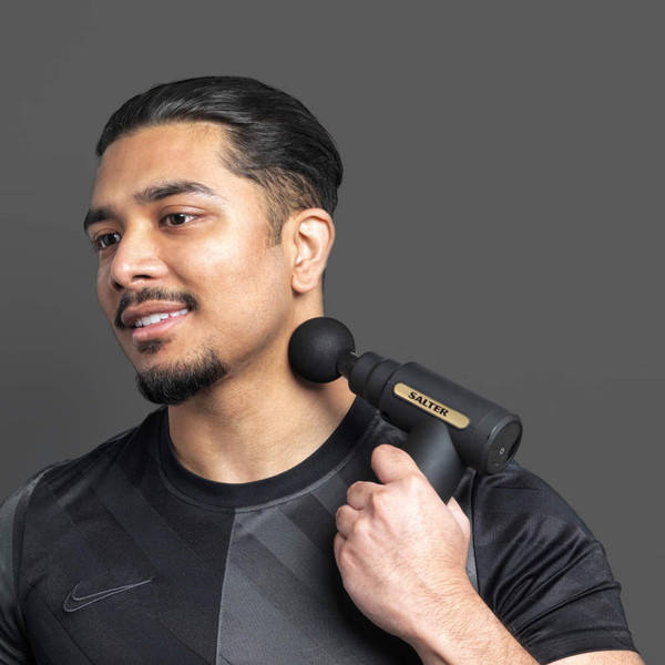 Black massage gun with round head in use on shoulder