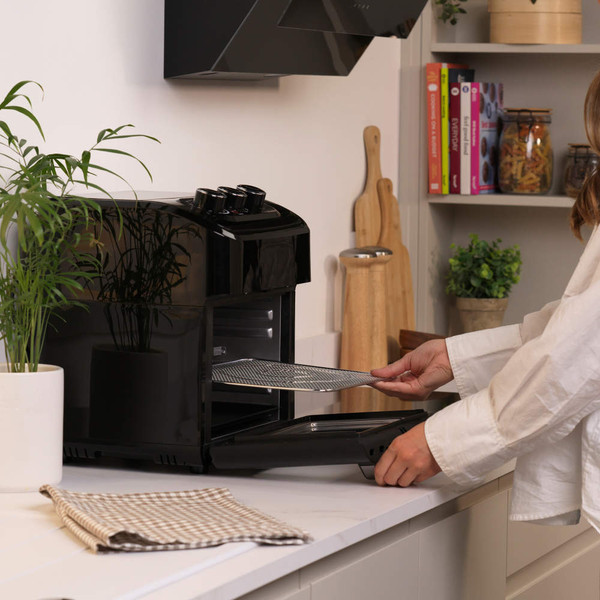 Person placing tray into black air fryer oven on kitchen counter