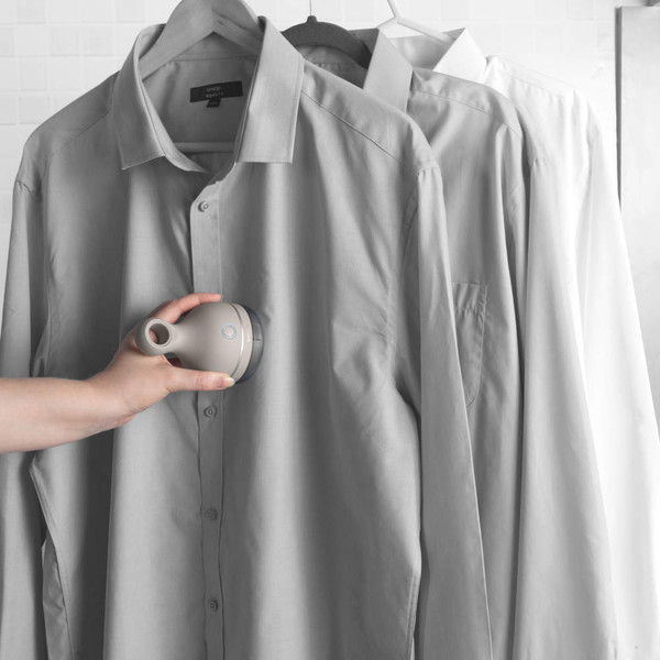 Hand-held garment steamer in use on grey shirt hanging beside other shirts
