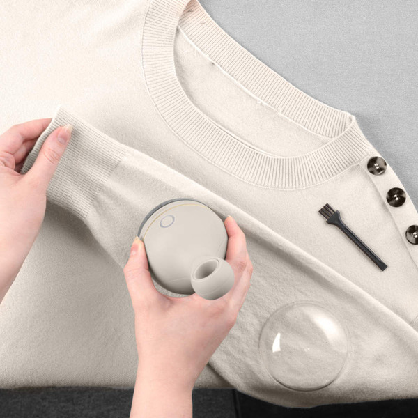 Hand using fabric shaver to remove bobbles from light beige jumper, with cleaning brush shown.