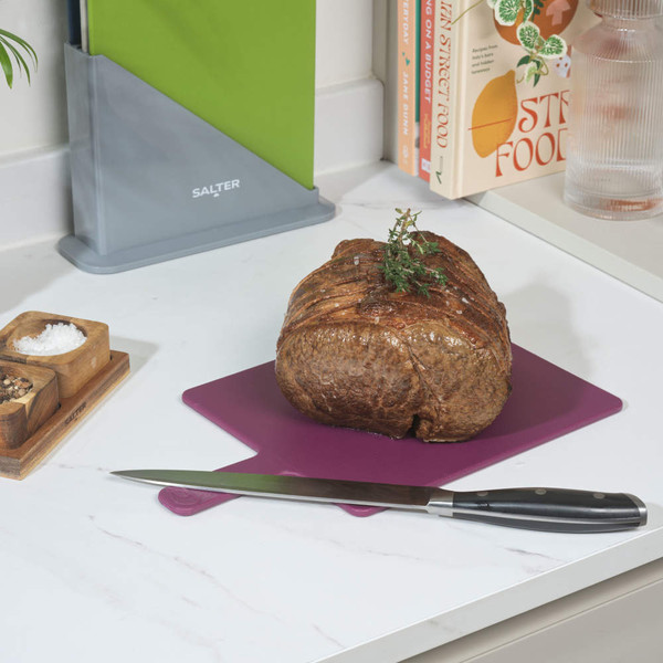 Cooked beef joint with herbs on purple chopping board, carving knife beside on kitchen worktop