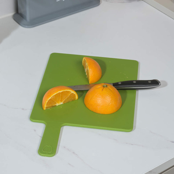 Knife slicing orange on green chopping board