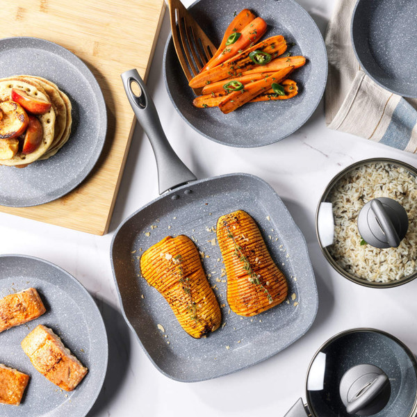 Grey non-stick cookware set with food, including grilled squash, carrots, salmon, rice, and pancakes.