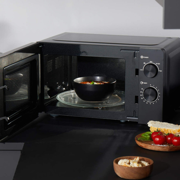 Black microwave oven with open door, heating soup bowl on glass turntable, kitchen setting