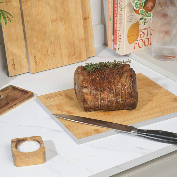 Kitchen scene with three bamboo chopping boards, roast beef, sliced lemons and limes, and water glasses