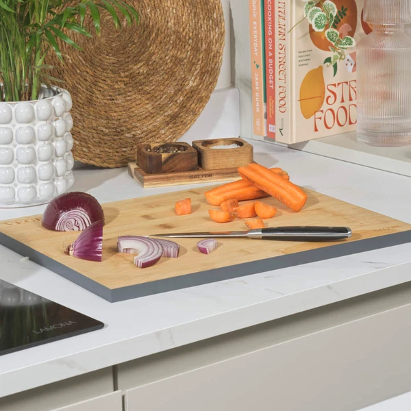 Bamboo chopping board with cut carrot and red onion on kitchen counter