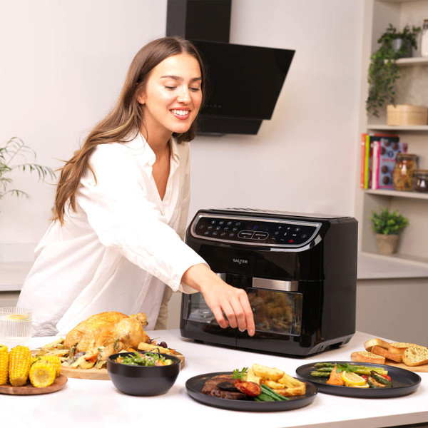 Salter black digital air fryer oven in kitchen scene with cooked dishes on table