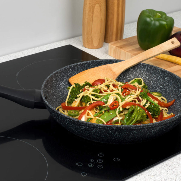 Black non-stick frying pan with stir fry noodles and vegetables on induction hob