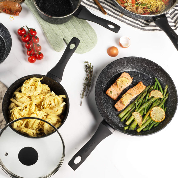 Set of three black non-stick frying pans, one with salmon and asparagus, one with omelette and spinach.