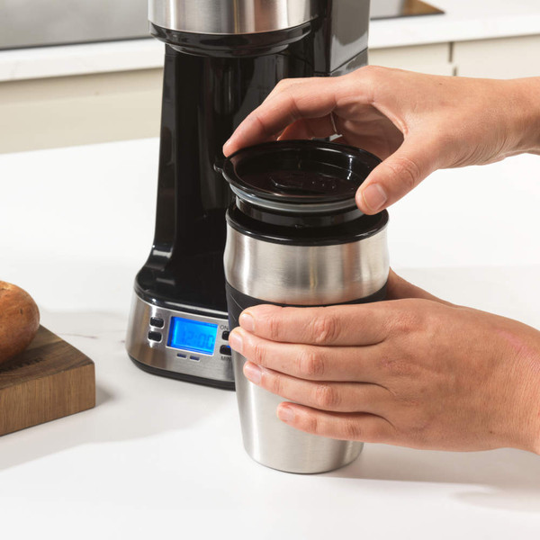 Single-serve silver coffee maker with travel mug, coffee grounds, and coffee pods shown.