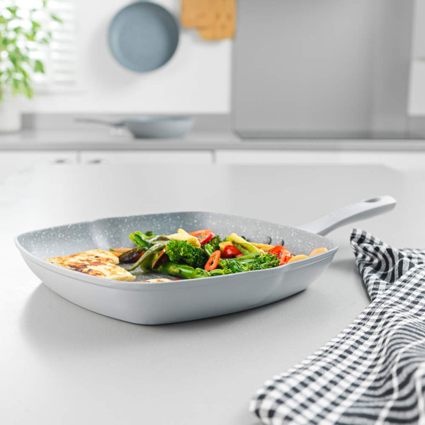 Silver frying pan with speckled coating, cooking mixed vegetables, angled on white surface