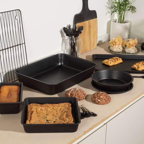 Set of black non-stick baking trays and cake tins on a kitchen counter