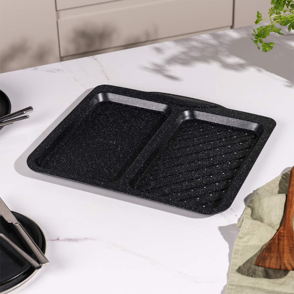 Black non-stick oven tray with divider and grill section, shown on kitchen counter