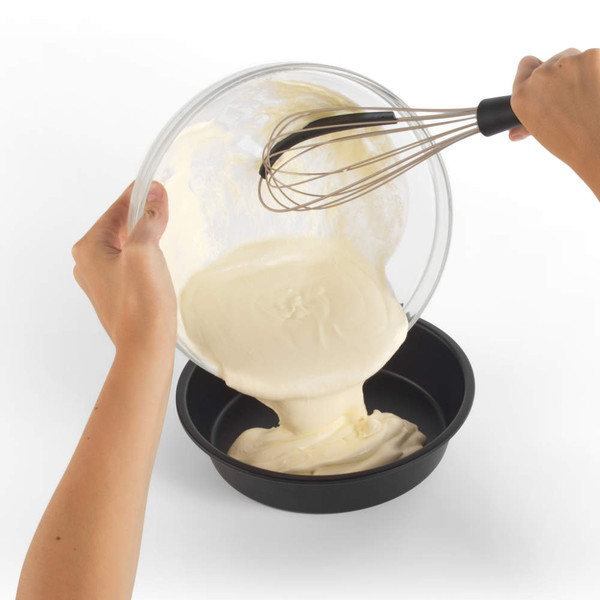 Pouring cake batter from glass bowl with whisk into round non-stick baking tin